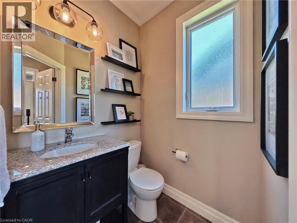 Vanity with a granite countertop and undermount sink, overhead lighting fixture, wall-mounted mirror, and a window with frosted glass - 913 Valebrook Court, Kitchener, ON - Indoor Photo Showing Bathroom