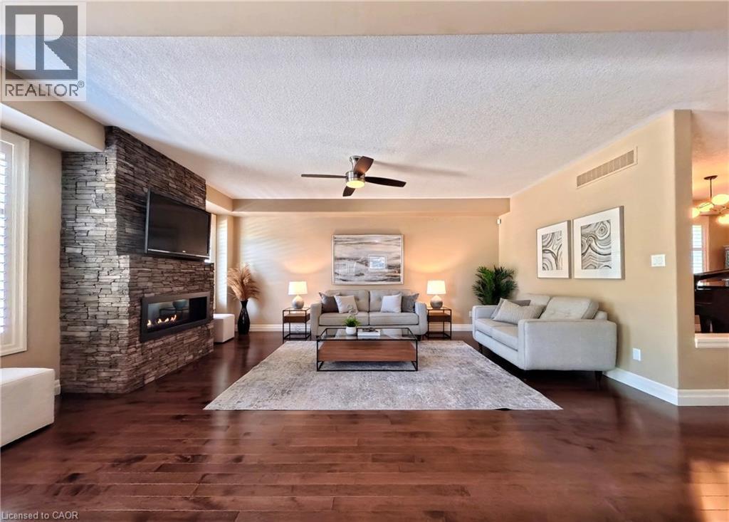 Spacious living room showcasing rich wood-finish flooring, a striking brick fireplace with integrated flat-screen television, and ceiling fan - 913 Valebrook Court, Kitchener, ON - Indoor Photo Showing Living Room With Fireplace