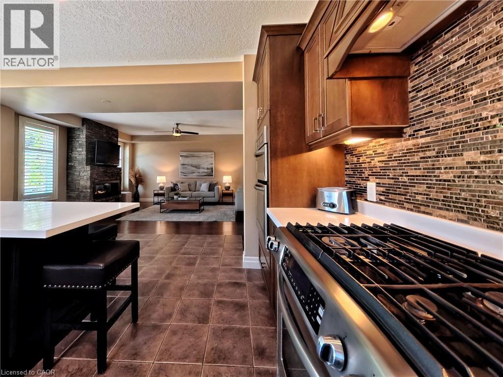 Stainless steel gas range with a tile backsplash, wood cabinetry, and a kitchen island with seating - 913 Valebrook Court, Kitchener, ON - Indoor Photo Showing Kitchen