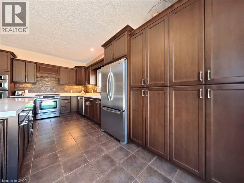 Kitchen featuring extensive wood-finish cabinetry, stainless steel appliances, a tile backsplash, and solid surface countertops - 913 Valebrook Court, Kitchener, ON - Indoor Photo Showing Kitchen