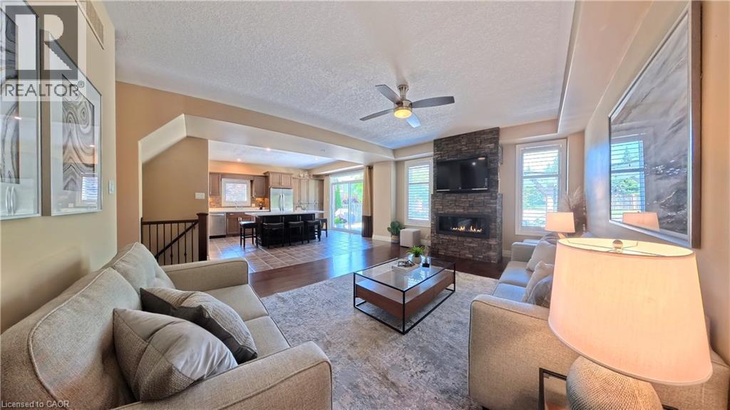 Spacious living area featuring a stacked stone fireplace, ceiling fan, and wood-finish flooring - 913 Valebrook Court, Kitchener, ON - Indoor Photo Showing Living Room With Fireplace