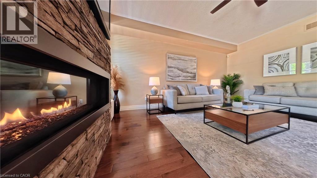 Sophisticated living room showcasing a linear fireplace with stacked stone surround, rich wood-finish flooring, and recessed ceiling lighting - 913 Valebrook Court, Kitchener, ON - Indoor Photo Showing Living Room With Fireplace