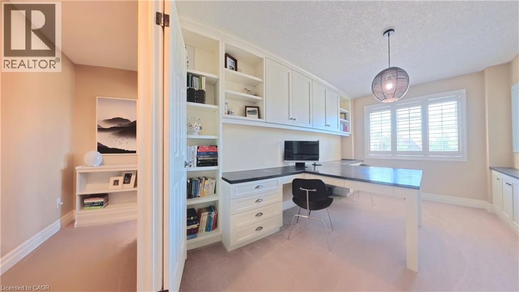 Sophisticated home office featuring built-in cabinetry with shelving and workspace, pendant lighting, desk with integrated storage drawers, ergonomic seating, light wood-finish flooring, and abundant - 913 Valebrook Court, Kitchener, ON - Indoor
