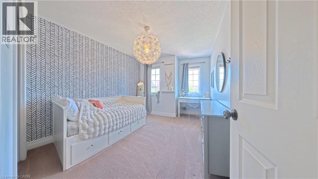 Patterned accent wall, flush mount chandelier, dual windows with curtains, built-in storage drawers, and carpeted flooring - 913 Valebrook Court, Kitchener, ON - Indoor Photo Showing Bedroom