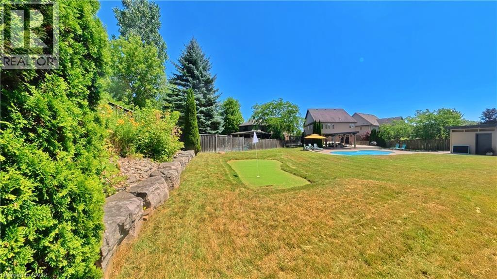 Expansive manicured lawn with mature tree-lined perimeter, stone retaining wall, and multiple outbuildings including a detached garage and storage structures - 913 Valebrook Court, Kitchener, ON - Outdoor With Backyard