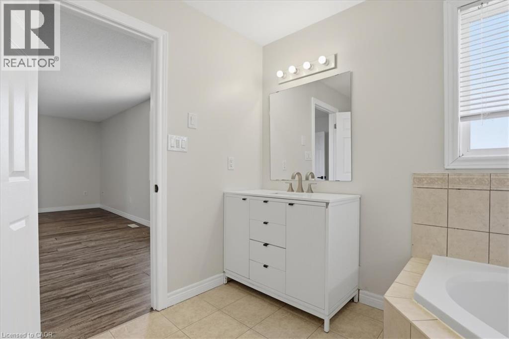 Spa-inspired primary bathroom featuring a white vanity with multiple drawers and brushed nickel hardware, a framed mirror with integrated lighting, tile surround accents, and a soaking tub - 43 Decaro Crescent, Cambridge, ON - Indoor Photo Showing Bathroom