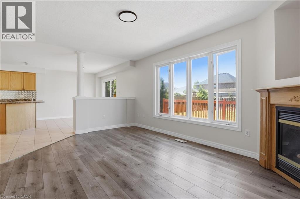 Bright open-concept living space featuring wood-finish flooring, abundant natural light from multi-panel sliding glass doors, and a fireplace with wood surround - 43 Decaro Crescent, Cambridge, ON - Indoor With Fireplace