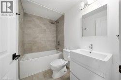 Modern bathroom featuring a white vanity with integrated rectangular sink and chrome faucet, ceramic tile flooring, a soaking tub with glass shower enclosure and tile surround, toilet, and large illum - 