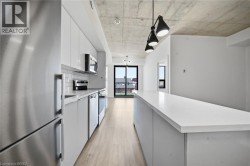 Modern galley kitchen featuring white cabinetry, stainless steel appliances including refrigerator and dishwasher, white quartz countertops, wood-finish flooring, and pendant lighting - 