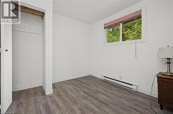 Wood-finish flooring with white baseboards, a single window with a privacy blind, and a built-in closet with shelving - 