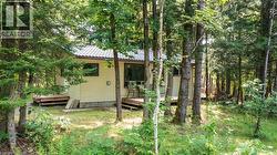 Wooded setting with mature trees, light-colored horizontal siding, and a dark-tiled roof - 