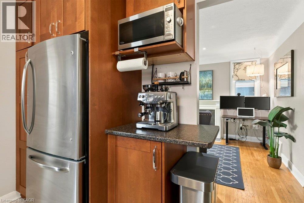 Modern kitchen featuring warm wood cabinetry, stainless steel appliances including a French-door refrigerator and microwave, granite countertops, and hardwood flooring throughout - 23 Kipling Road, Hamilton, ON - Indoor Photo Showing Kitchen