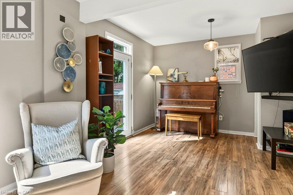 Versatile living space featuring warm wood-finish flooring, built-in shelving with display cabinetry, an upright piano, pendant lighting, wall-mounted television, and a decorative plate wall arrangeme - 23 Kipling Road, Hamilton, ON - Indoor