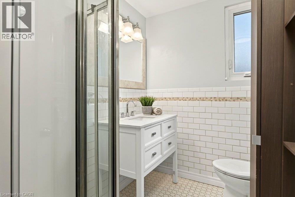Spa-inspired bathroom featuring a walk-in shower enclosure with brushed nickel framing, white subway tile walls with decorative tile trim, a white vanity with multiple drawers and chrome hardware, pol - 23 Kipling Road, Hamilton, ON - Indoor Photo Showing Bathroom