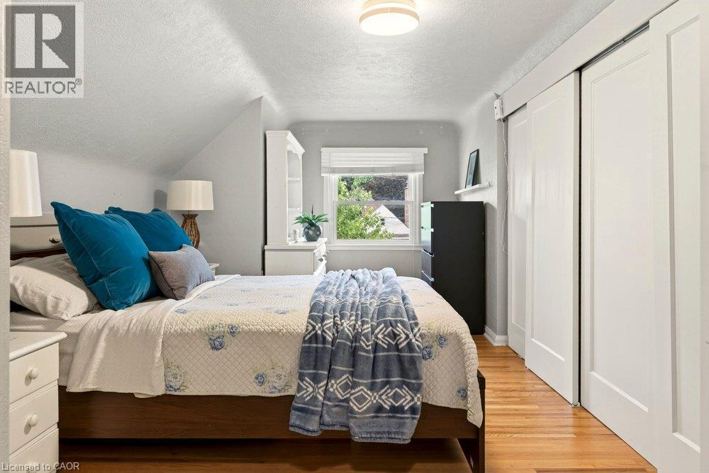 Bright, light-filled bedroom featuring hardwood flooring, a large window with natural outdoor views, white built-in closet doors, and a ceiling-mounted light fixture - 23 Kipling Road, Hamilton, ON - Indoor Photo Showing Bedroom