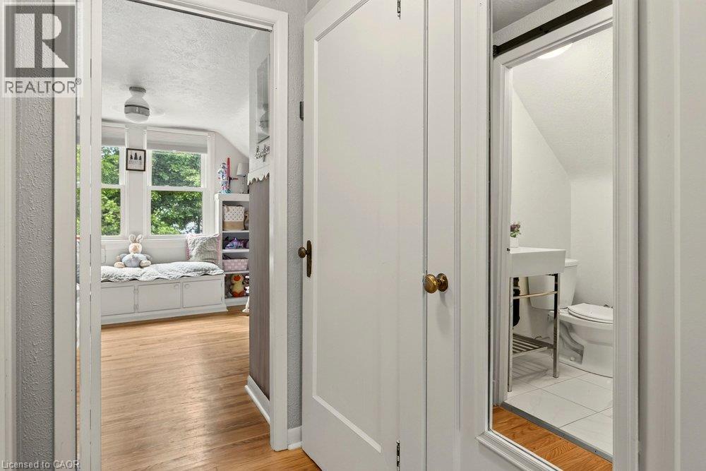 Hallway with white painted doors and wood-finish flooring, providing access to a bedroom with large windows, a full bathroom with white subway tile and fixtures, and additional living spaces throughou - 23 Kipling Road, Hamilton, ON - Indoor