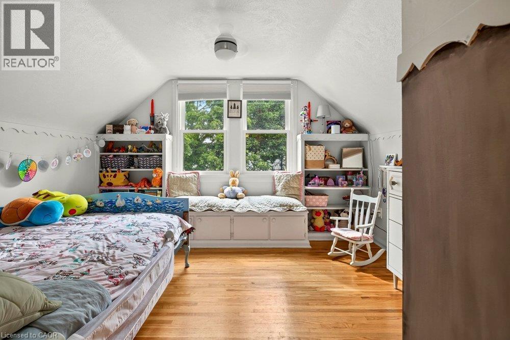 Charming attic bedroom featuring sloped ceilings, wood-finish flooring, and abundant natural light from a multi-pane window - 23 Kipling Road, Hamilton, ON - Indoor Photo Showing Bedroom