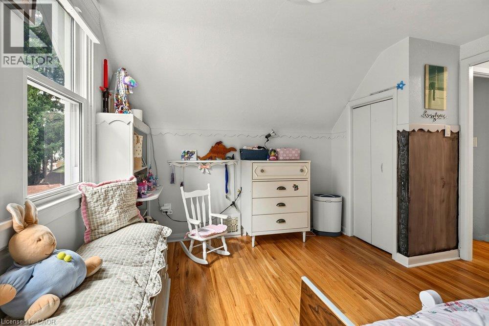 Bright, light-filled bedroom showcasing hardwood flooring, a large multi-pane window with natural outdoor views, and sloped ceiling architecture - 23 Kipling Road, Hamilton, ON - Indoor