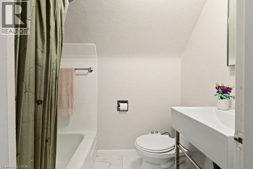 Clean, bright bathroom featuring a white ceramic vessel sink with a contemporary wall-mounted faucet, white subway tile surround, porcelain flooring, an enclosed shower/tub combination with a neutral - 23 Kipling Road, Hamilton, ON - Indoor Photo Showing Bathroom