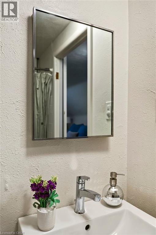 Modern bathroom vanity featuring a sleek chrome faucet, white ceramic sink with integrated countertop, polished metal-framed medicine cabinet with mirrored doors, and neutral textured wall finishes - 23 Kipling Road, Hamilton, ON - Indoor Photo Showing Bathroom