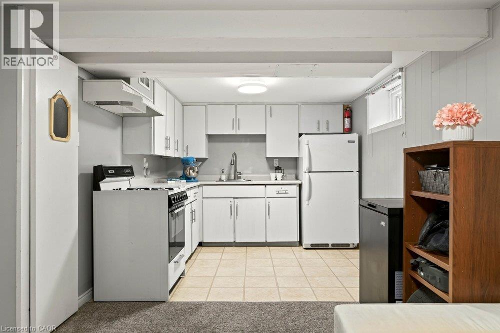 Galley kitchen featuring white cabinetry, stainless steel appliances including a gas range and refrigerator, tile flooring, and ample counter and storage space - 23 Kipling Road, Hamilton, ON - Indoor Photo Showing Kitchen