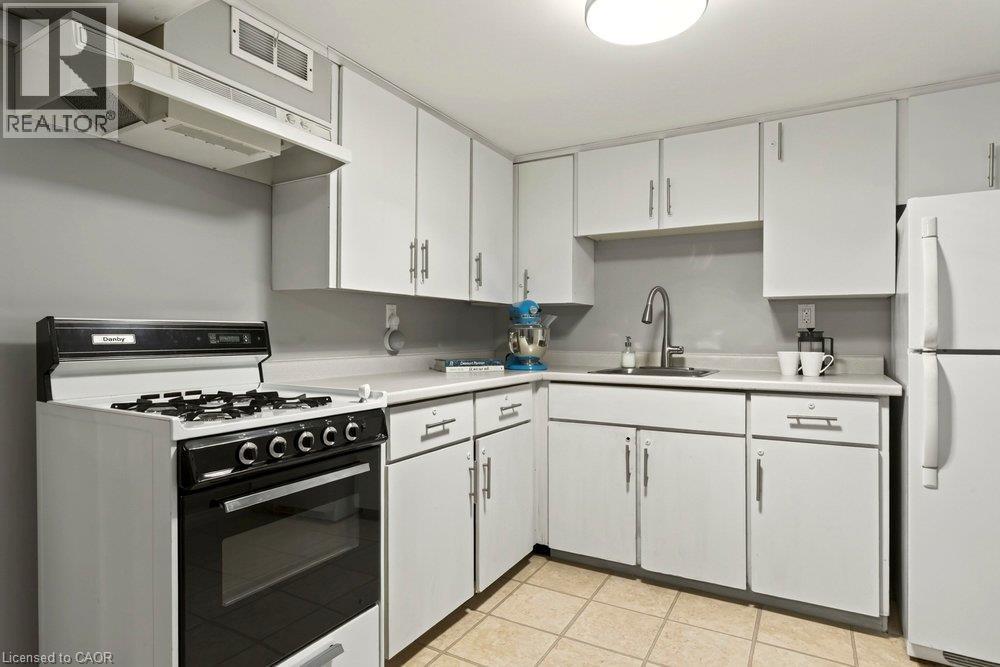 Updated kitchen featuring white cabinetry with stainless steel hardware, black gas range with multiple burners and convection oven, stainless steel sink with single-handle faucet, tile flooring, and w - 23 Kipling Road, Hamilton, ON - Indoor Photo Showing Kitchen