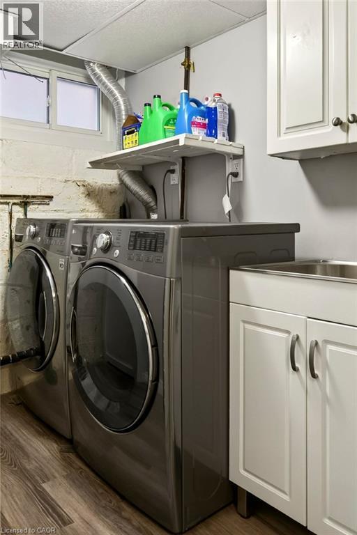 Laundry area featuring wood-finish flooring, white cabinetry, and a utility sink - 23 Kipling Road, Hamilton, ON - Indoor Photo Showing Laundry Room