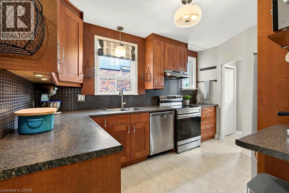 Kitchen featuring wood cabinetry, dark tile backsplash, stainless steel appliances, and a double basin sink - 23 Kipling Road, Hamilton, ON - Indoor Photo Showing Kitchen With Stainless Steel Kitchen With Double Sink