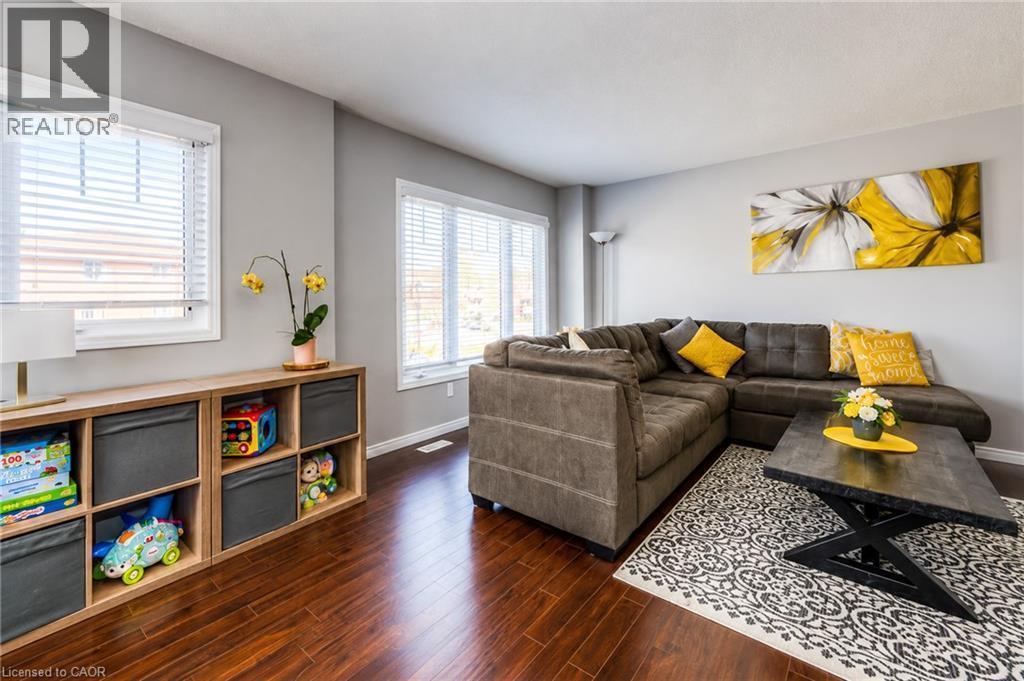 Spacious living area featuring wood-finish flooring, light grey wall paint, and multiple windows with white blinds - 750 Lawrence Street Unit# 86, Cambridge, ON - Indoor Photo Showing Living Room