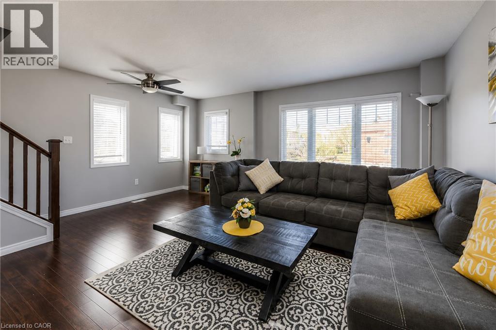 Spacious living area featuring wood-finish flooring, multiple windows with blinds, a ceiling fan, and a wood staircase with dark balusters - 750 Lawrence Street Unit# 86, Cambridge, ON - Indoor Photo Showing Living Room