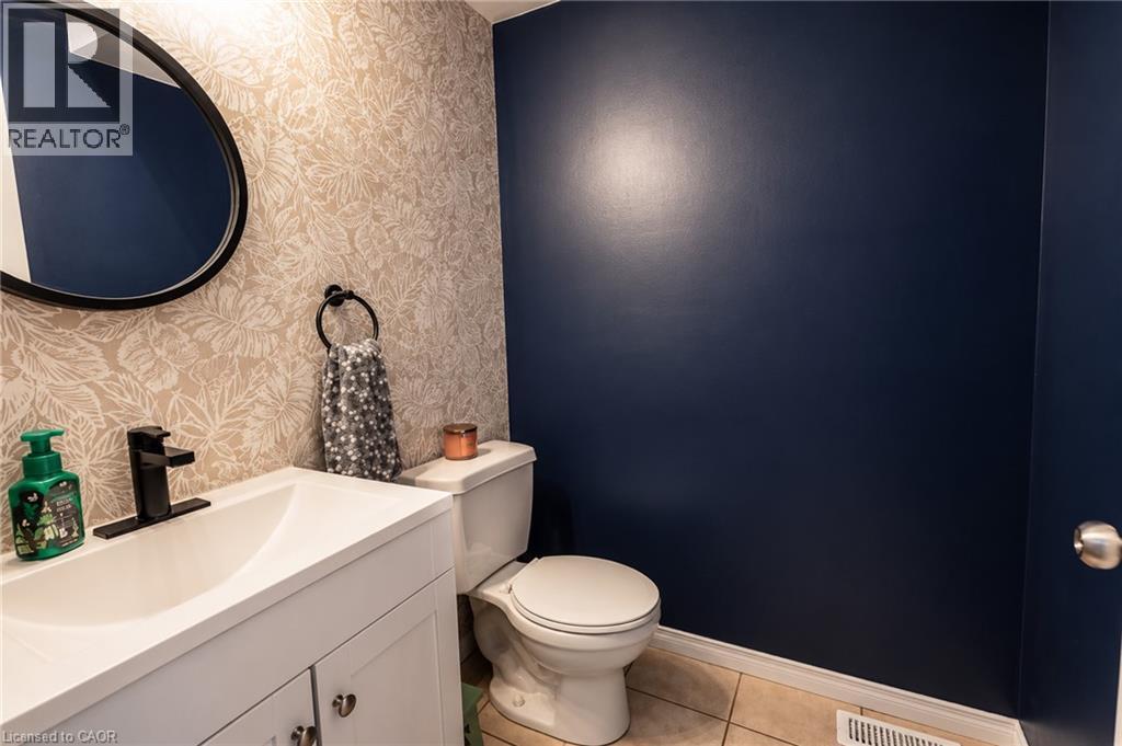 Powder room with a white vanity, black faucet, circular mirror, and patterned wallpaper accent wall - 750 Lawrence Street Unit# 86, Cambridge, ON - Indoor Photo Showing Bathroom