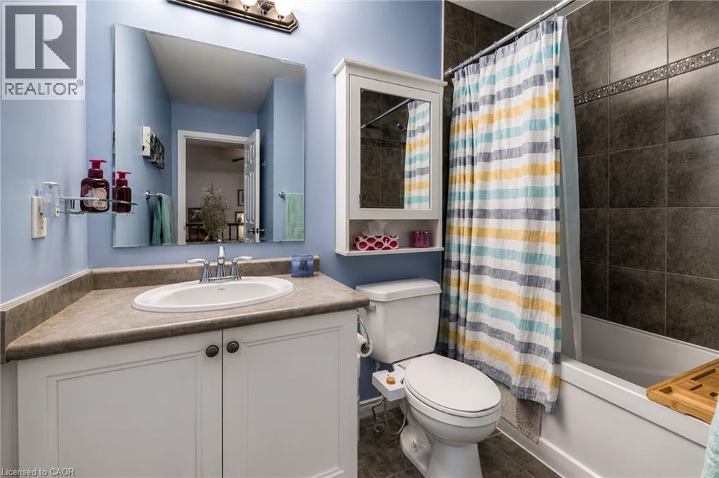 Bathroom featuring a white vanity with paneling and dark hardware, a spacious countertop, an oval undermount sink, a white toilet, and a shower-over-tub combination with dark tile surround and decorat - 750 Lawrence Street Unit# 86, Cambridge, ON - Indoor Photo Showing Bathroom