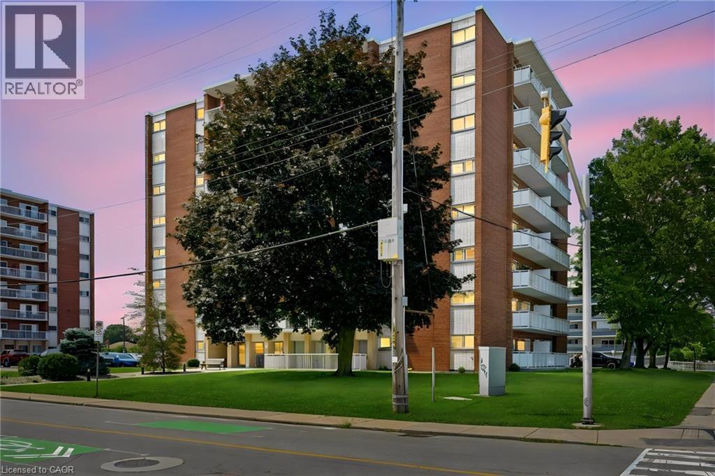 Multi-story building featuring brick and light-colored siding, individual balconies, and a manicured lawn - 8 Woodman Drive S Unit# 708, Hamilton, ON - Outdoor With Balcony With Facade