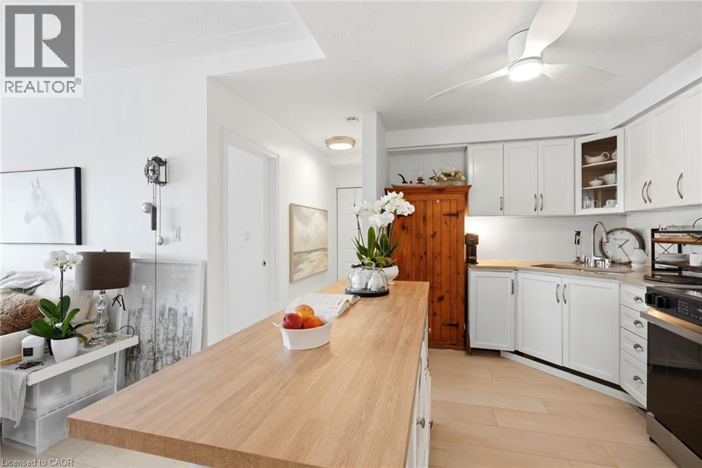 Kitchen featuring a ceiling fan with integrated lighting, white cabinetry, light countertops, and wood-finish flooring - 8 Woodman Drive S Unit# 708, Hamilton, ON - Indoor Photo Showing Kitchen