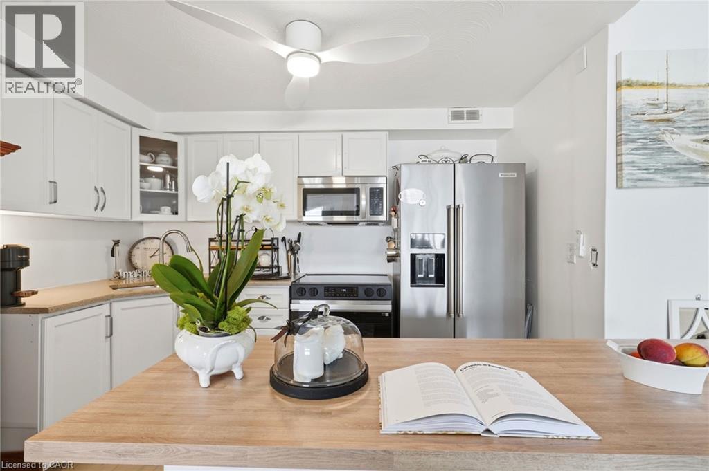 White cabinetry, stainless steel appliances, wood-finish countertops, built-in microwave, and ceiling fan - 8 Woodman Drive S Unit# 708, Hamilton, ON - Indoor Photo Showing Kitchen With Stainless Steel Kitchen