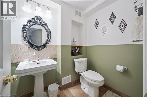 Pedestal sink with dual faucets, decorative framed mirror, wall-mounted light fixture, and tile flooring - 817 Acadia Drive, Hamilton, ON - Indoor Photo Showing Bathroom