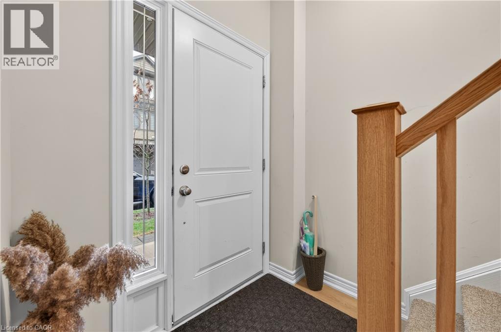 White paneled entry door with sidelight, wood-finish flooring, and natural wood staircase newel post and handrail - 19 Picardy Drive Unit# 13, Hamilton, ON - Indoor Photo Showing Other Room