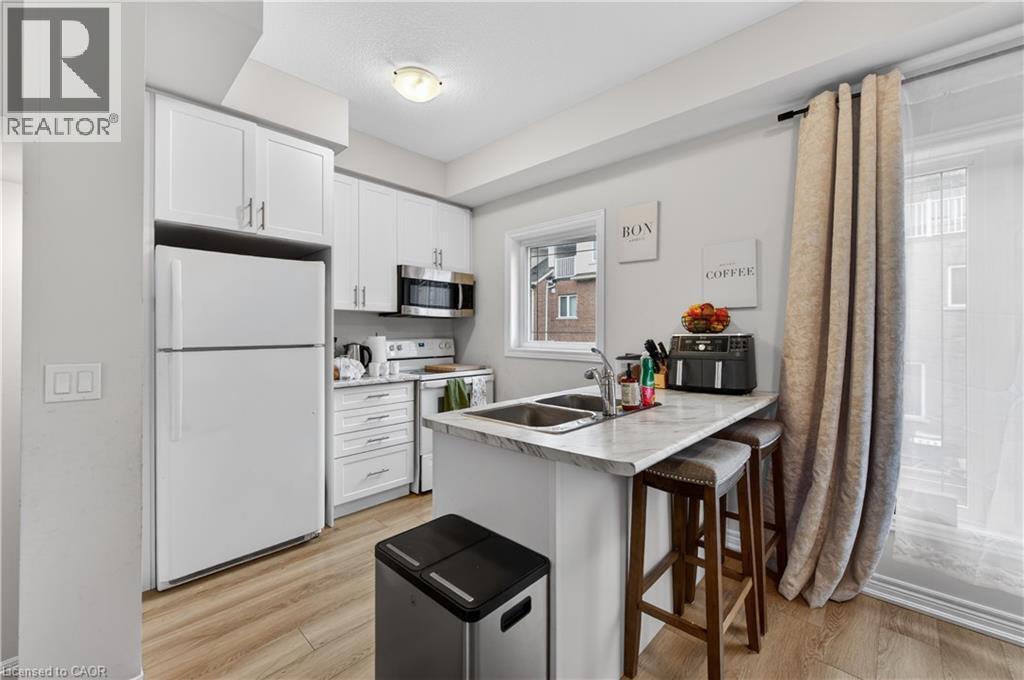 Modern kitchen featuring white cabinetry, stainless steel microwave, light-toned wood-finish flooring, and a double-basin sink - 19 Picardy Drive Unit# 13, Hamilton, ON - Indoor Photo Showing Kitchen With Double Sink
