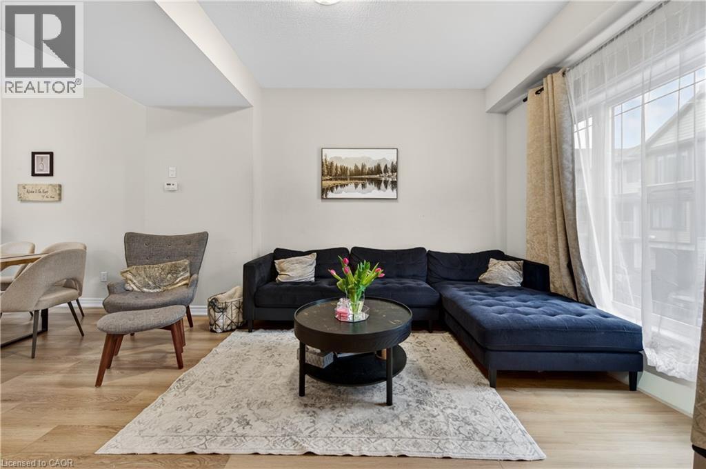Living area featuring light-toned walls, wood-finish flooring, and a large window - 19 Picardy Drive Unit# 13, Hamilton, ON - Indoor Photo Showing Living Room