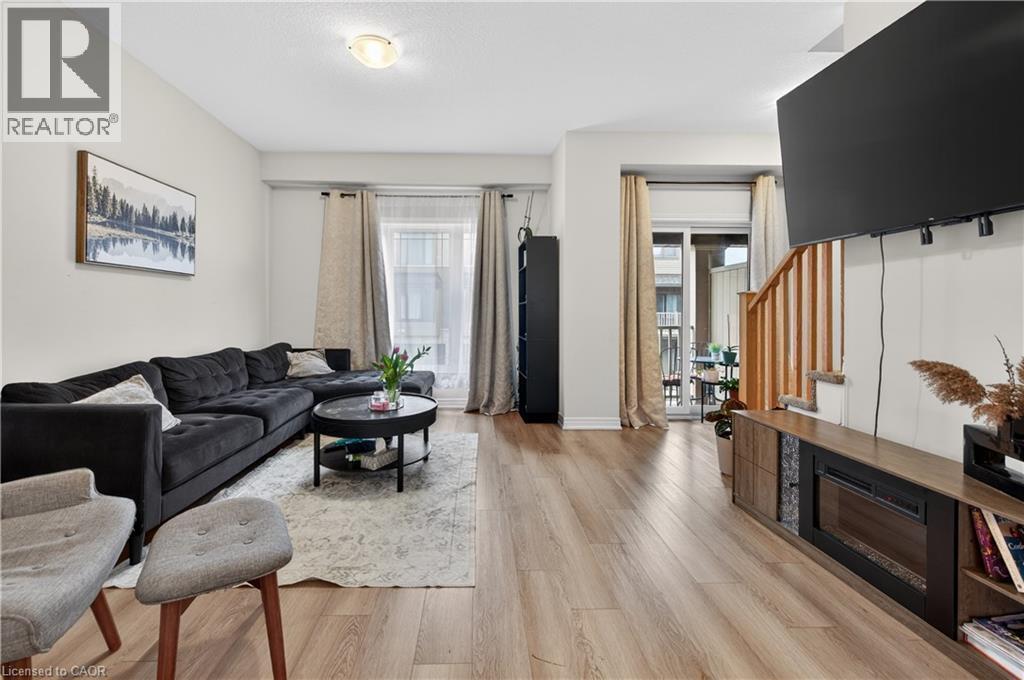 Open-concept living area featuring wood-finish flooring, a built-in electric fireplace, and a sliding glass door leading to a balcony - 19 Picardy Drive Unit# 13, Hamilton, ON - Indoor Photo Showing Living Room With Fireplace