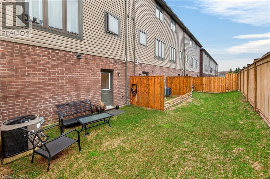 Expansive grassy area featuring a full privacy fence, brick exterior, and an exterior door - 19 Picardy Drive Unit# 13, Hamilton, ON - Outdoor