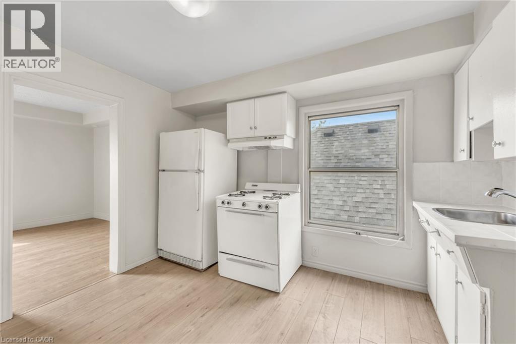 Kitchen featuring white cabinetry, wood-finish flooring, a white gas range, a white refrigerator, and a stainless steel sink - 1367 Cannon Street E, Hamilton, ON - Indoor Photo Showing Kitchen