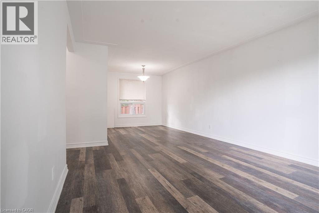 Spacious interior room showcasing rich wood-finish flooring with varied plank toning, bright natural light from a multi-pane window, clean white walls, and ceiling-mounted lighting fixture - 695 Glen Forrest Boulevard Unit# Upper, Waterloo, ON - Indoor Photo Showing Other Room
