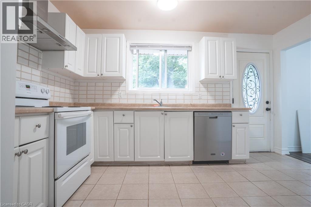 White cabinetry with brushed nickel hardware, light-toned countertops, tile backsplash, stainless steel dishwasher, and a window above the sink - 695 Glen Forrest Boulevard Unit# Upper, Waterloo, ON - Indoor Photo Showing Kitchen