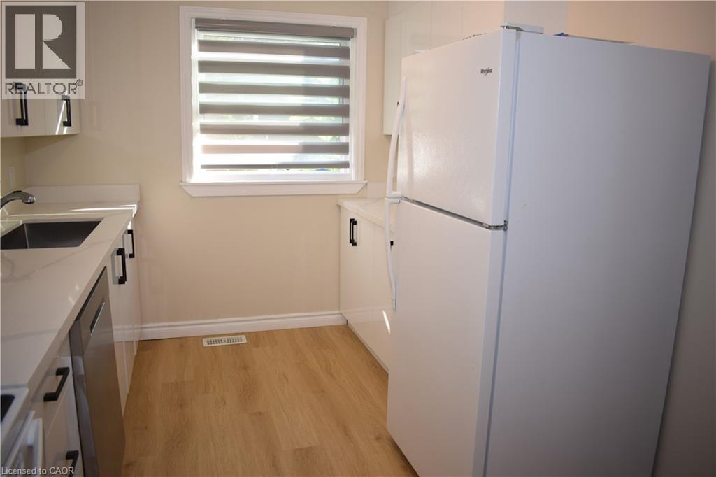 White cabinetry with dark hardware, a stainless steel sink, light-toned wood-finish flooring, a white refrigerator, and a window with blinds - 655 Albert Street Unit# A, Waterloo, ON - Indoor Photo Showing Kitchen
