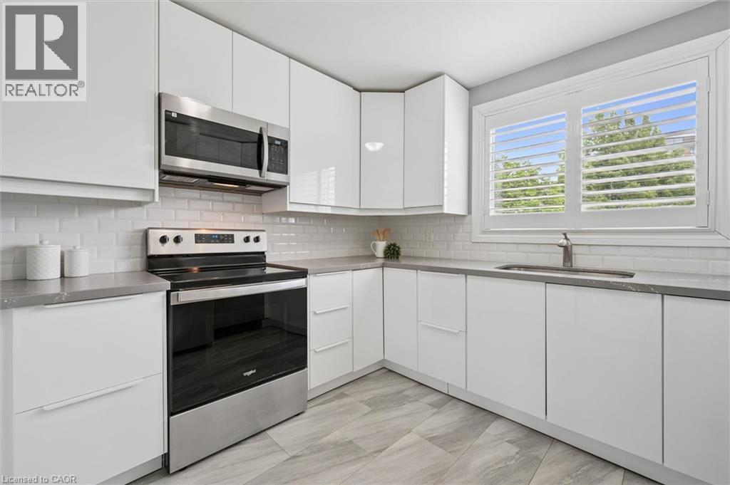 White flat-panel cabinetry, stainless steel appliances, light gray countertops, subway tile backsplash, and light-toned tile flooring - 60 Elmsdale Drive Unit# 25, Kitchener, ON - Indoor Photo Showing Kitchen