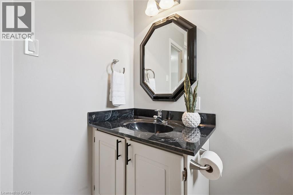 Vanity featuring a dark stone countertop, integrated sink, and white cabinetry with dark hardware - 60 Elmsdale Drive Unit# 25, Kitchener, ON - Indoor Photo Showing Bathroom