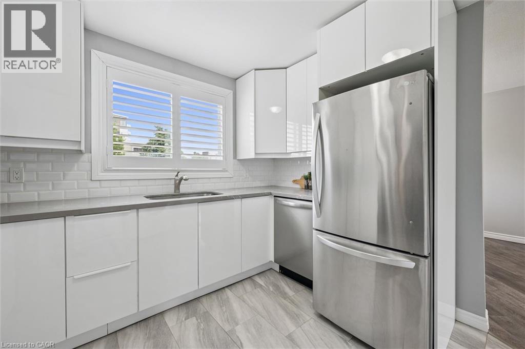 White cabinetry, stainless steel appliances, subway tile backsplash, light-toned countertops, and wood-finish flooring - 60 Elmsdale Drive Unit# 25, Kitchener, ON - Indoor Photo Showing Kitchen With Stainless Steel Kitchen
