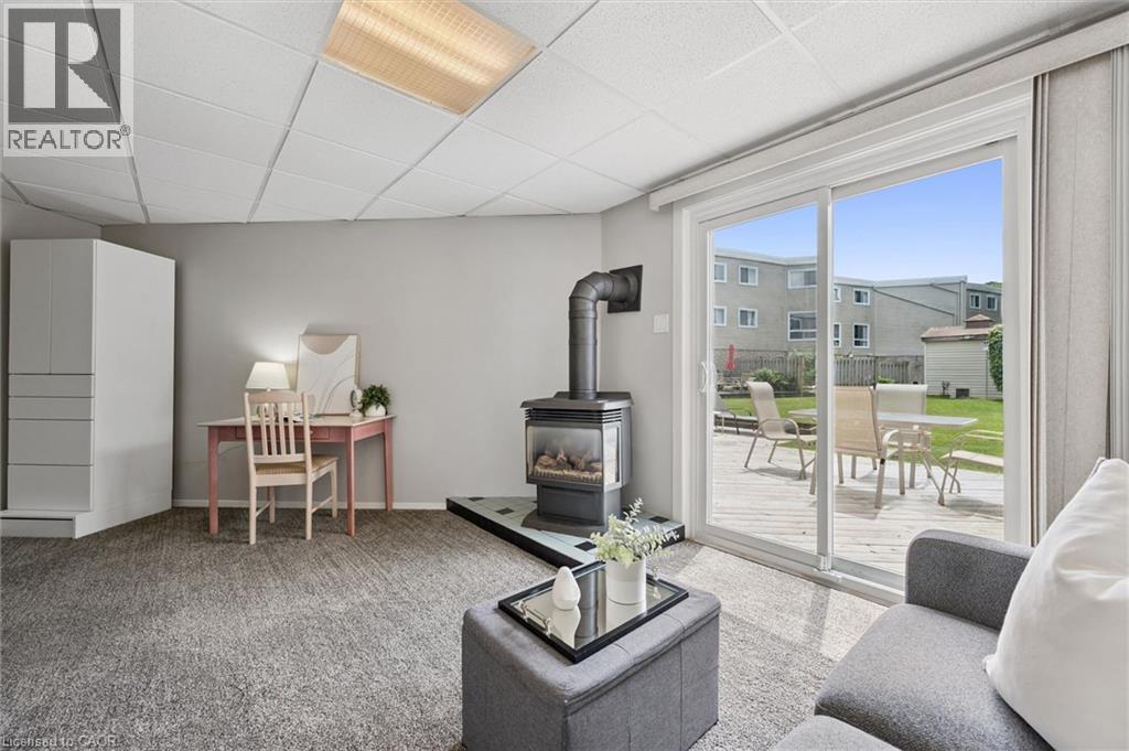 Sliding glass doors opening to an exterior wood deck, a freestanding wood-burning stove with a glass door, light grey wall paint, and recessed ceiling lighting - 60 Elmsdale Drive Unit# 25, Kitchener, ON - Indoor