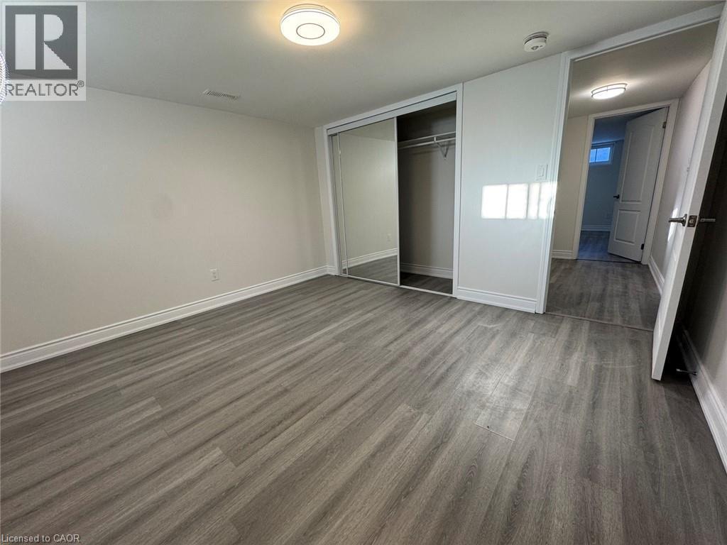 Grey wood-finish flooring, white walls, flush mount ceiling lighting, and sliding mirrored closet doors - 15 Pinecrest Drive Unit# Lower, Kitchener, ON - Indoor Photo Showing Other Room